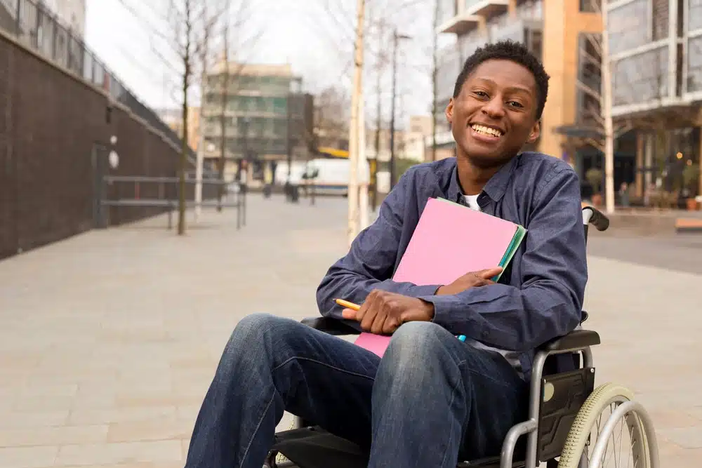 happy young disabled man in a wheelchair holding folders